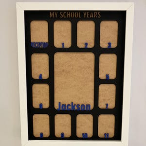 May include: A white rectangular picture frame with a black mat board featuring the text MY SCHOOL YEARS at the top. It contains twelve small photo slots labeled Reception through 11 in blue, plus a larger central slot labeled Jackson in blue.
