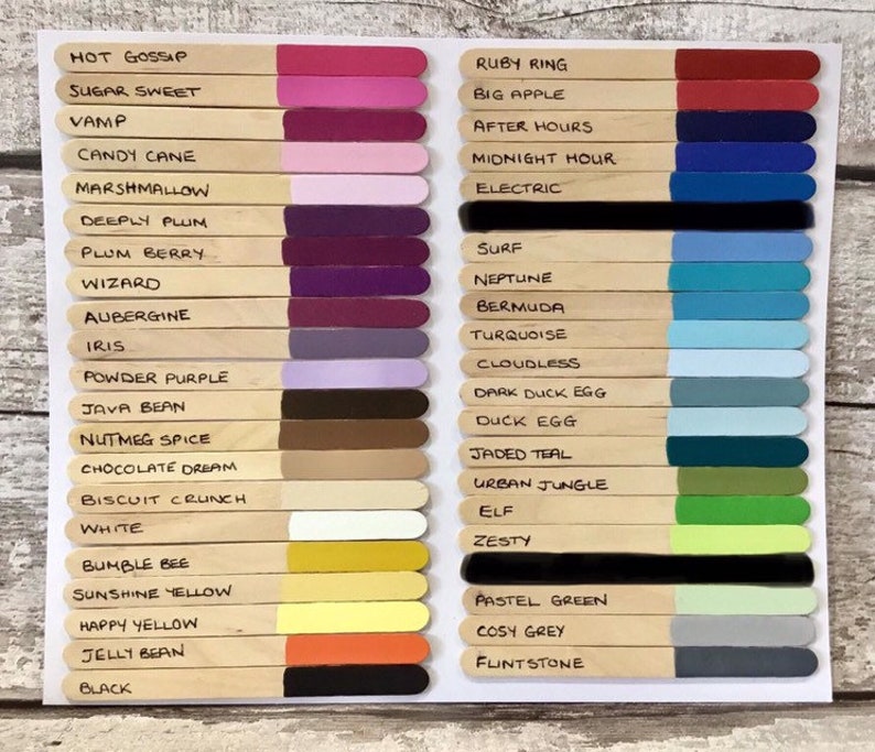 May include: A color chart featuring two columns of wooden craft sticks, each tipped with a unique paint color and labeled with names like Hot Gossip, Ruby Ring, and Black. The sticks are arranged in rows, displaying a wide spectrum of shades.