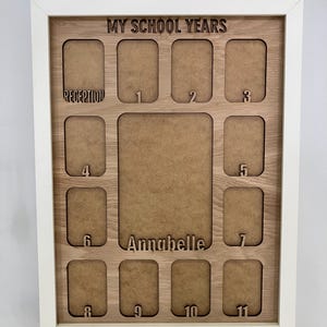 May include: A white-framed wooden display board titled MY SCHOOL YEARS with cutouts for photos. It features a large central space labeled Annabelle and smaller slots labeled Reception and numbers 1 through 11 for school year progression.