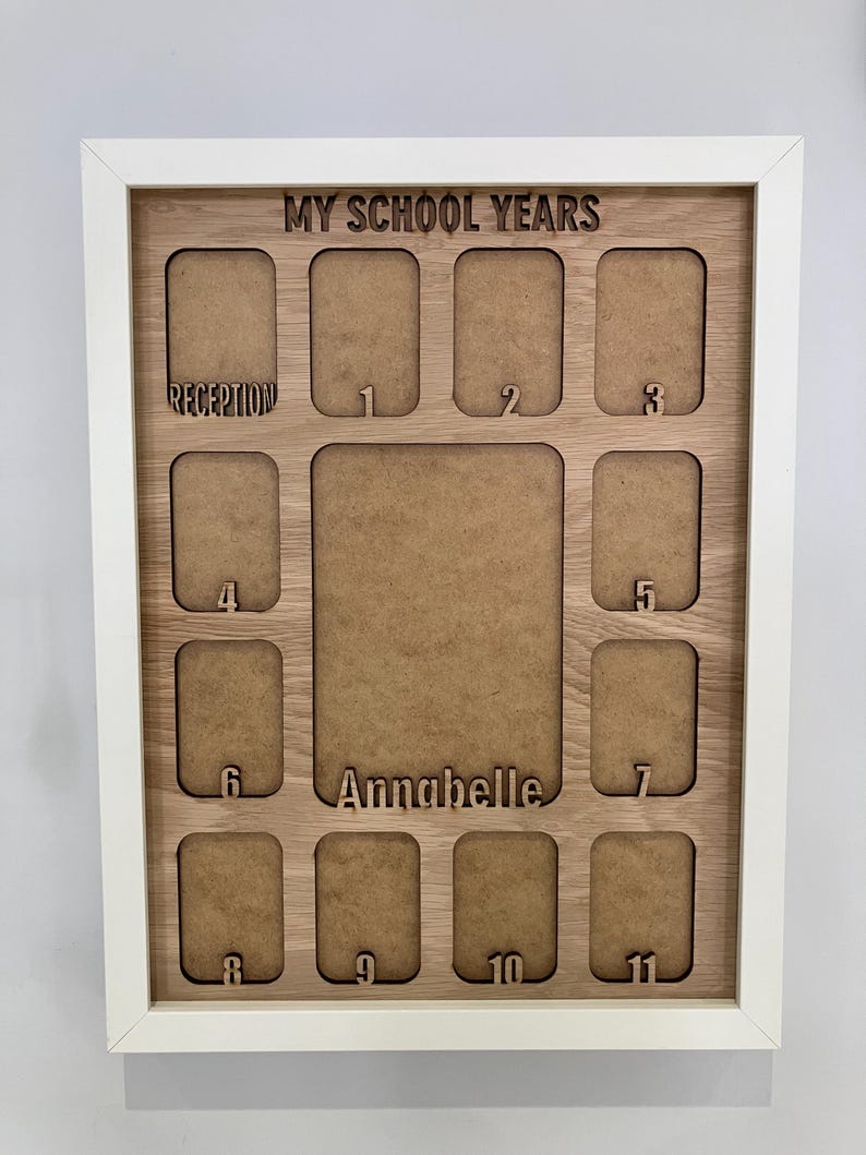 May include: A white-framed wooden display board titled MY SCHOOL YEARS with cutouts for photos. It features a large central space labeled Annabelle and smaller slots labeled Reception and numbers 1 through 11 for school year progression.