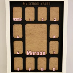 May include: A white rectangular frame containing a black mat with the text MY SCHOOL YEARS at the top. It features twelve small photo slots labeled Reception through 11 in pink, and a larger central slot with the name Morgan in pink lettering.