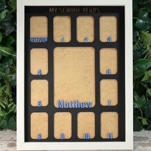 May include: A white rectangular picture frame with a black mat board featuring the text MY SCHOOL YEARS at the top. The frame contains twelve small photo slots labeled Reception through 11 in blue, and a central slot with the name Matthew.