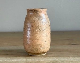 May include: A small, light brown ceramic vase with a textured surface.