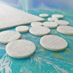 May include: A close-up of white felt circles of varying sizes on a blue and gold marbled surface. The circles are arranged in a pattern, with the largest circle in the center.