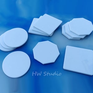 May include: A set of white ceramic coasters in various shapes, including round, square, and octagonal. The coasters are stacked on top of each other and are arranged on a blue surface. The text "HW Studio" is visible in the lower right corner of the image.