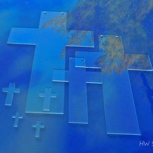 May include: A collection of transparent acrylic crosses in various sizes, arranged against a gradient blue background. The crosses have a simple, clean design, with small holes at the top for hanging. The image is labeled "HW studio".