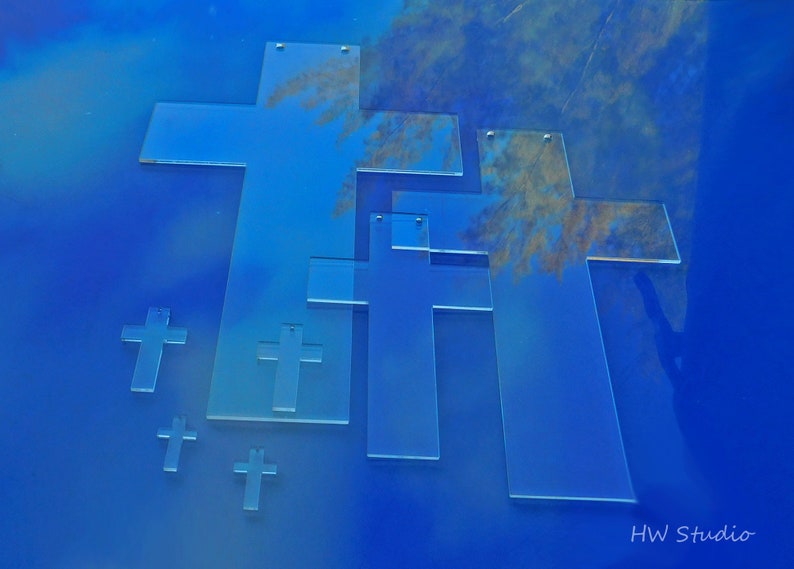May include: A collection of transparent acrylic crosses in various sizes, arranged against a gradient blue background. The crosses have a simple, clean design, with small holes at the top for hanging. The image is labeled "HW studio".