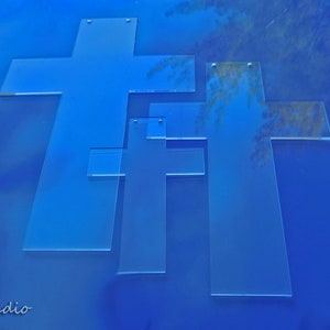 May include: Three transparent, light blue crosses of varying sizes are arranged on a solid blue background. The crosses are made of a clear material, and the image has a clean, modern aesthetic. The image is a studio shot.