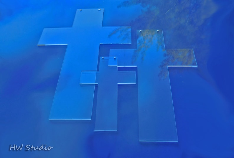 May include: Three transparent, light blue crosses of varying sizes are arranged on a solid blue background. The crosses are made of a clear material, and the image has a clean, modern aesthetic. The image is a studio shot.