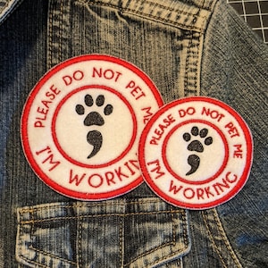 May include: Two red and white embroidered patches with a paw print and semicolon. The text on the patches reads "Please do not pet me I'm working".