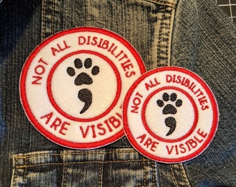 May include: Two red and white embroidered patches on a blue denim jacket. The patches say "Not All Disabilities Are Visible" and feature a paw print and a semicolon.