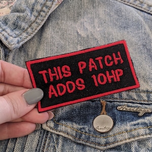 May include: A black and red embroidered patch that says "This Patch Adds 10HP" on a denim jacket.