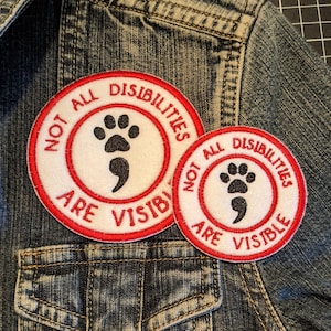 May include: Two red and white embroidered patches on a blue denim jacket. The patches say "Not All Disabilities Are Visible" and feature a paw print and a semicolon.