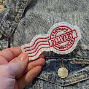 May include: White embroidered patch with red stitching. The patch features a red and white striped design with the words "EXPRESS DELIVERY NORTH POLE" in a circle.