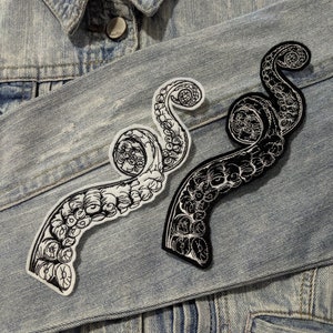May include: Two black and white embroidered iron-on patches of an octopus tentacle design on a blue denim jacket.