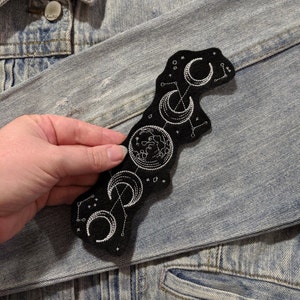 May include: A black felt patch with white embroidery of a crescent moon and stars. The patch is sewn onto a light blue denim jacket.