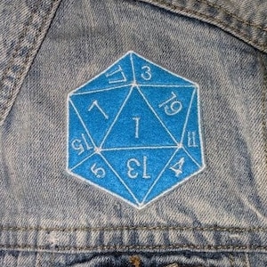 May include: A blue denim jacket with a blue and white embroidered 20-sided die patch. The die shows the numbers 1, 3, 5, 13, 19, and 4.