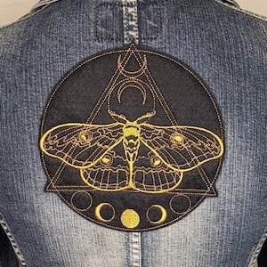 May include: A black denim jacket with a circular embroidered patch featuring a moth, a triangle, and a crescent moon. The patch is outlined in gold thread.
