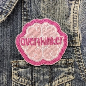 May include: Pink embroidered brain patch with the text "overthinker" on a denim jacket.