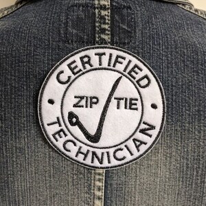 May include: A white, round patch with black text and a black checkmark. The text reads "Certified Zip Tie Technician".