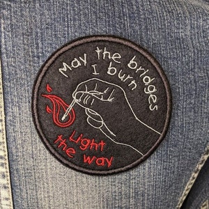 May include: Black and white embroidered patch with red flame and text that reads "May the bridges I burn light the way".