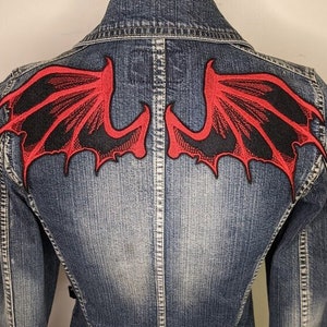 May include: A denim jacket with a red and black embroidered dragon wing design on the back.