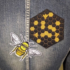 May include: A denim jacket with two embroidered patches. One patch is a yellow and black bee, the other is a black and gold honeycomb with bees.