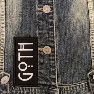 May include: A blue denim jacket with a black patch that says "GOTH" in white lettering.