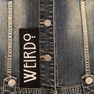 May include: A blue denim jacket with a black patch that says "WEIRDO." in white lettering.
