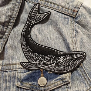 May include: Black and white embroidered whale patch on a blue denim jacket.