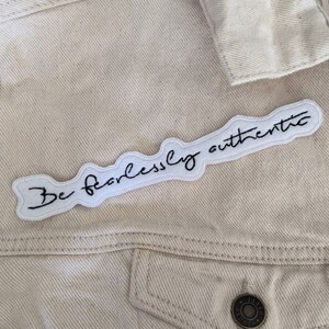 May include: A white denim jacket with a white embroidered patch that says "Be fearlessly authentic".