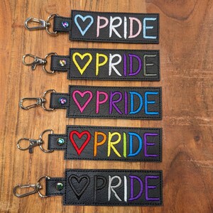 May include: Five black leather keychains with a heart and the word "PRIDE" embroidered in different colors. The colors are light blue, yellow, pink, red, and white.