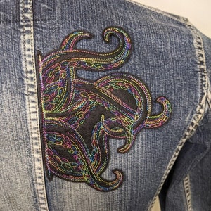 May include: A denim jacket with a colourful embroidered octopus patch on the back. The octopus is outlined in black thread and filled with rainbow coloured thread.