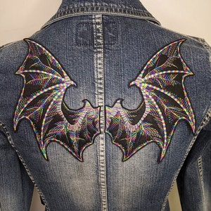 May include: A denim jacket with a pair of iridescent black dragon wings embroidered on the back. The wings have a rainbow iridescent sheen.