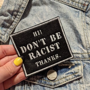 May include: A black square patch with white text that reads "Hi! Don't Be Racist. Thanks."