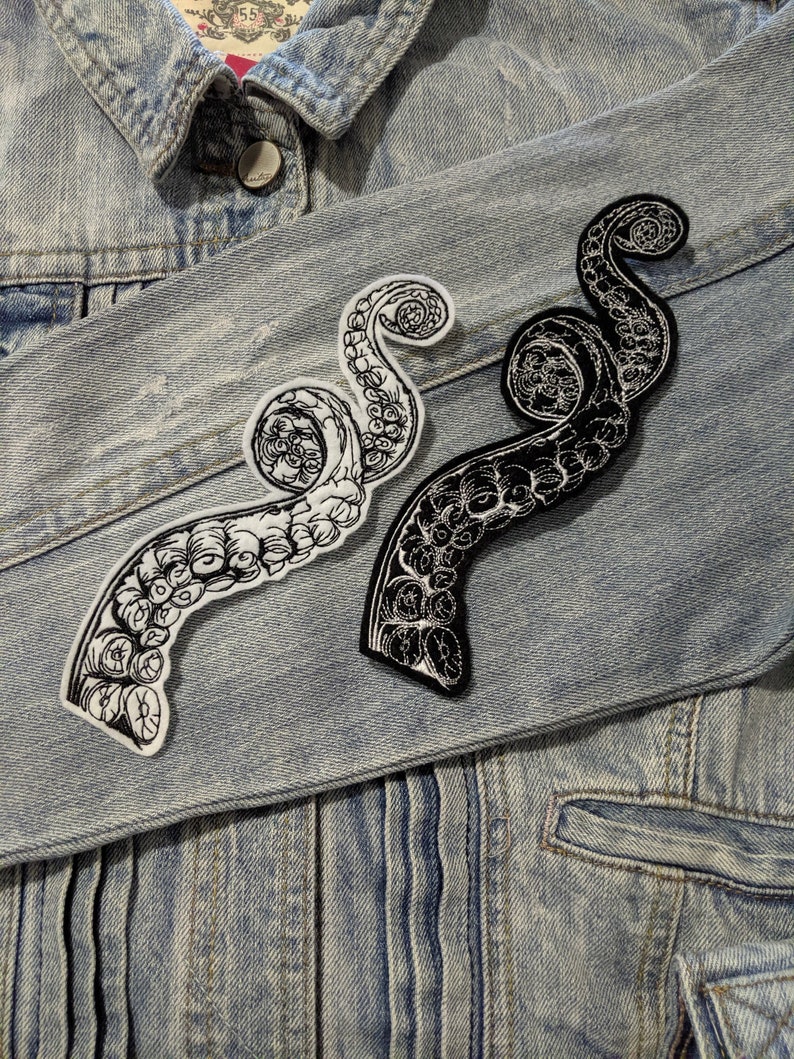 May include: Two black and white embroidered iron-on patches of an octopus tentacle design on a blue denim jacket.