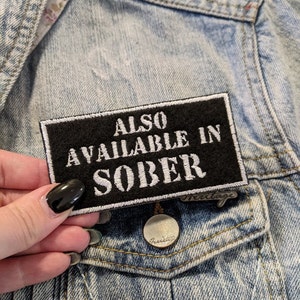 May include: Black patch with white text that reads "ALSO AVAILABLE IN SOBER" on a denim jacket.