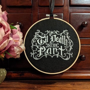 May include: A black embroidery hoop with white embroidery that reads "Til Death Do Us Part" in a gothic font.