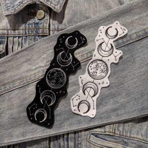 May include: Two embroidered patches with a celestial theme. One patch is black with white embroidery and the other is white with black embroidery. Both patches feature moons, stars, and geometric shapes.