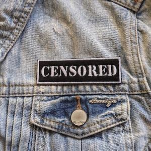 May include: A black and white embroidered patch with the word "CENSORED" on a denim jacket.