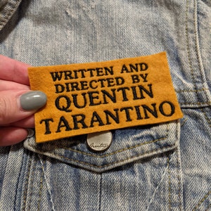 May include: A yellow felt patch with black embroidered text that reads "Written and Directed by Quentin Tarantino".