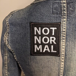 May include: A denim jacket with a black patch that says "NOT NORMAL" in white letters.