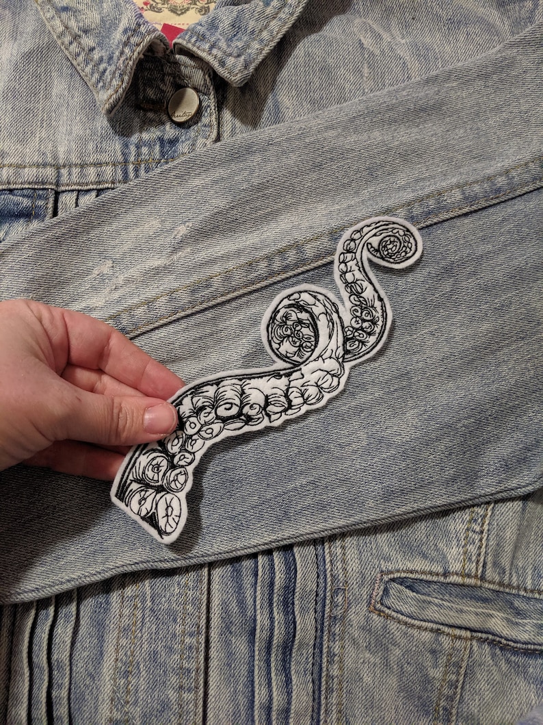 May include: A white denim jacket with a black and white embroidered octopus tentacle patch sewn on the left side of the jacket.