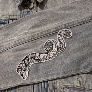 May include: A black and white octopus tentacle iron-on patch on a light blue denim jacket.
