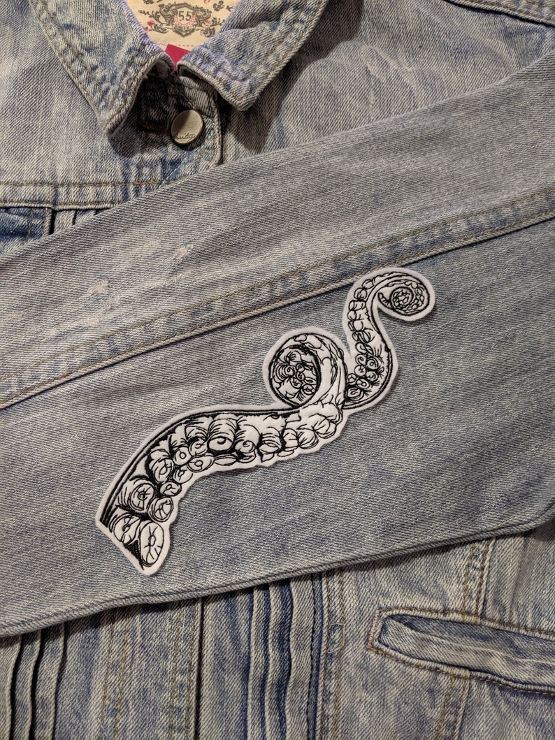May include: A black and white octopus tentacle iron-on patch on a light blue denim jacket.