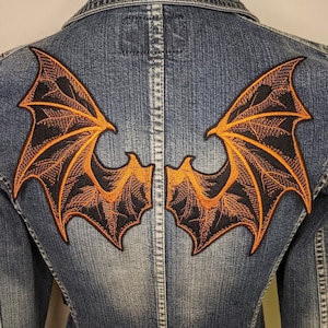 May include: Two black and orange embroidered patches of dragon wings, sewn onto a denim jacket.
