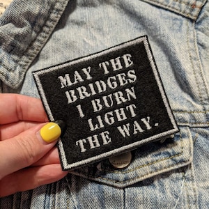 May include: Black and white embroidered patch with the text "May the bridges I burn light the way."