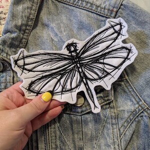 May include: A black and white embroidered dragonfly patch on a denim jacket.