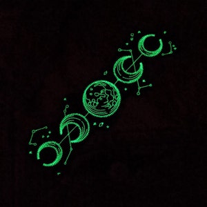 May include: A green glow-in-the-dark design of a planet and three crescent moons connected by lines and dots on a black background.