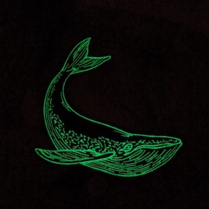 May include: A green glow-in-the-dark embroidered patch of a whale. The whale is facing left and has a detailed design.